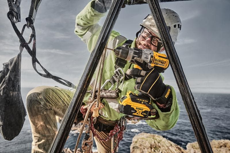 DEWALT DCD996P2, DCD996P2-QW drill used outdoors by worker; sea and rocks in background. Photography category.