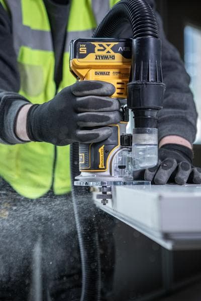 DEWALT DCW604NT-XJ, DCW604NT router in use, worker guides tool on edge with dust extraction. Photography category.