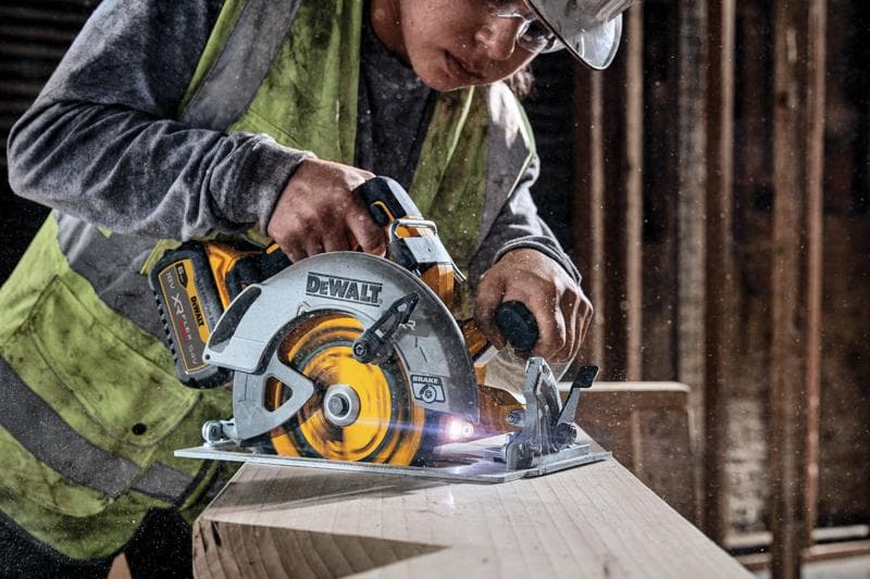 DEWALT cordless circular saw cutting wood, used by a worker wearing a vest in a construction setting.