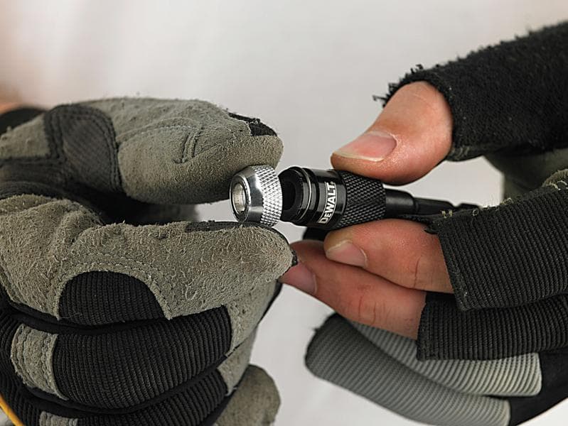 Gloved hands holding and adjusting a DEWALT drill bit holder.