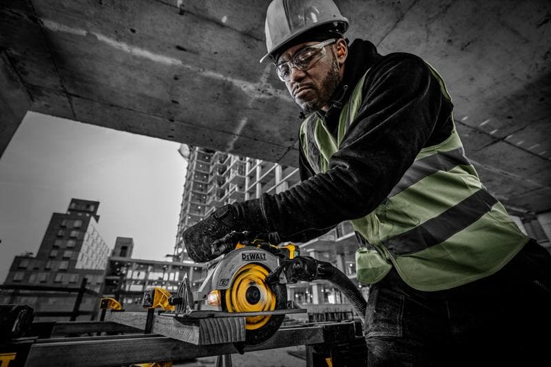 Person using a DEWALT circular saw DCS565NT on a construction site, wearing safety gear and cutting wood.