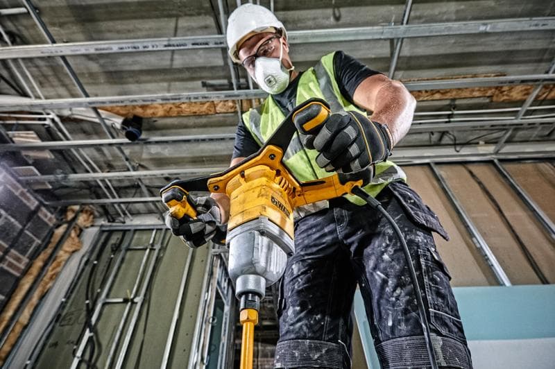 Person using DEWALT DWD241 mixer drill at a construction site, wearing safety gear and gloves.