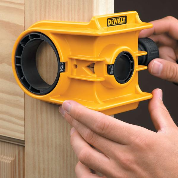 A person is using a yellow DEWALT door lock installation kit to align and mark a hole on a wooden door frame.