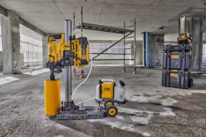A DEWALT core drilling machine with a yellow cylindrical drill attachment and connected water tank is positioned on the floor of a concrete construction site. In the background, scaffolding and DEWALT branded stackable storage boxes are visible.