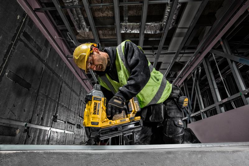 Worker using a DEWALT DCN890P2 nailer in a construction setting, wearing a helmet and safety vest.