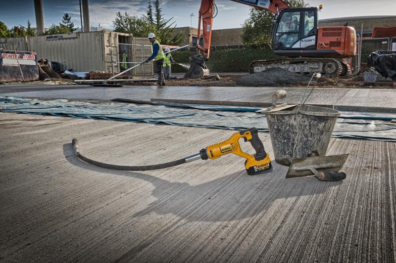 DEWALT cordless tool on a concrete site with bucket and trowel. Construction workers and excavator in background.