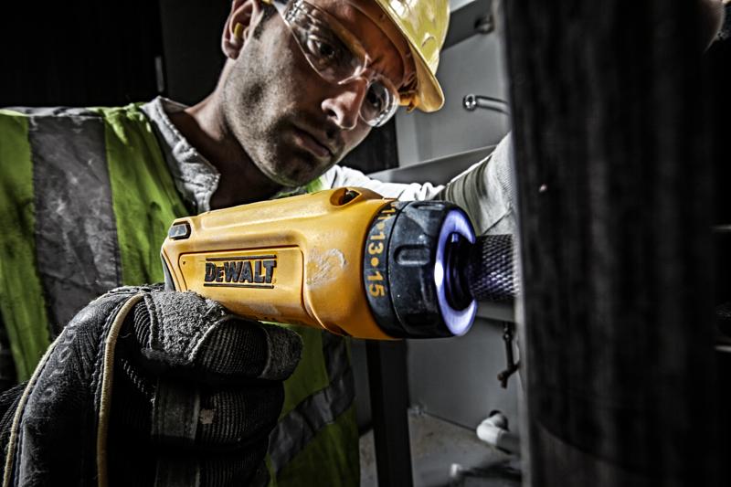 Person using yellow DEWALT DCF680G2 screwdriver with glove in industrial setting.