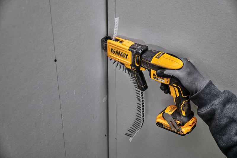 DEWALT DCF6202 screw gun driving screws into drywall, held by a gloved hand against a wall panel.