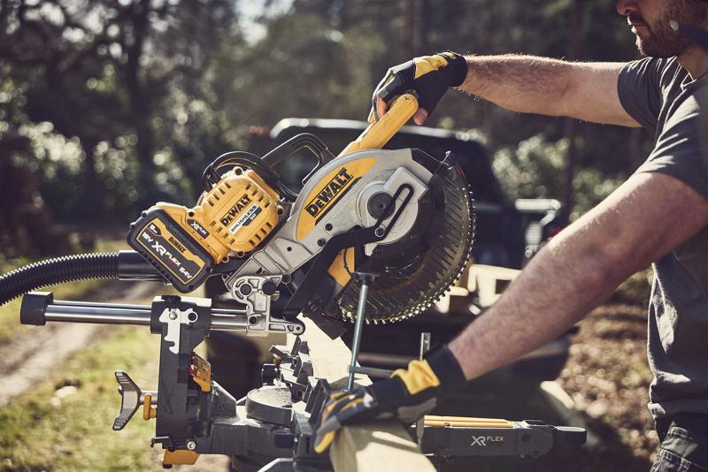Person using a DEWALT cordless mitre saw to cut wood outdoors; yellow and black tool with XR FLEXVOLT battery.