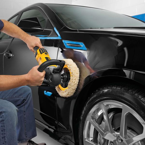 Person uses a DEWALT polisher to buff a black car’s fender in a garage.